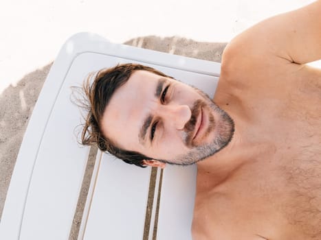 Young man lies on a sun lounger on the beach in the shade. High quality photo