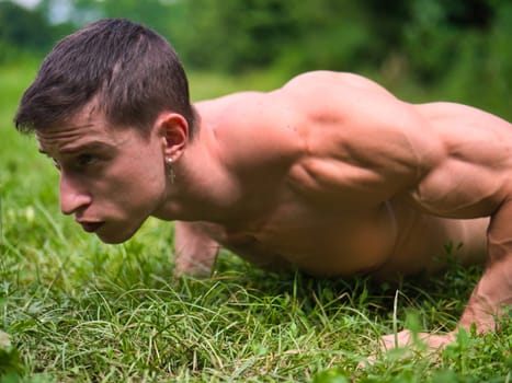 Close-up of topless young sportsman doing exercise for pecs in summer, in a park