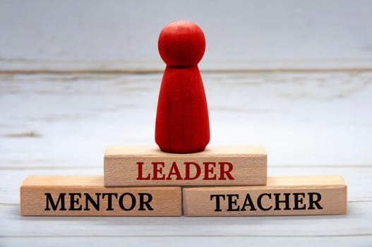 Leader, Mentor and Teacher text on wooden blocks with red figure on top. Leadership concept.