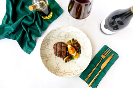 Exquisite serving of beef steak on a white plate with a glass of wine on a white background