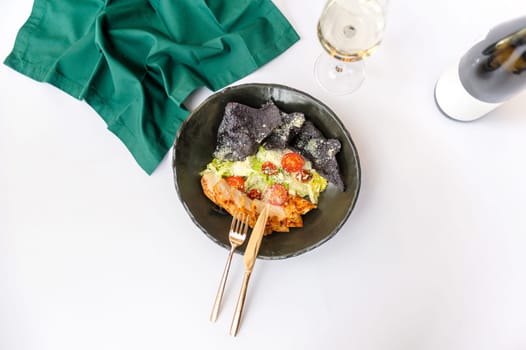 Exquisite serving Caesar salad with chicken on a black plate on a white background