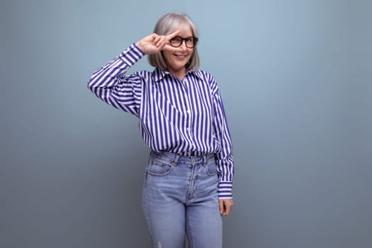 smiling 60s woman with gray hair in a stylish look is flirting on a bright studio background with copy space.