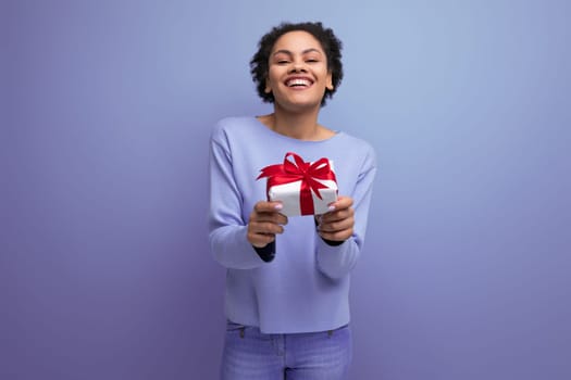 positive young brunette lady with afro curls holds out a gift box.