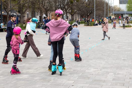 Ukraine. Kyiv. 23.04.2023. children, teenagers playing roller skates with friends outdoors. lot of children, kids go rollerblading, learn roller-skating with an adult instructor, having break in shade