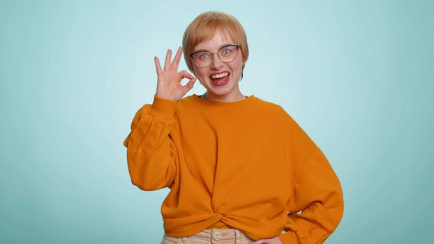 Ok. Joyful happy young woman in sweater looking approvingly at camera showing approve feedback gesture like sign positive something good. Pretty girl alone on blue background. People sincere emotion