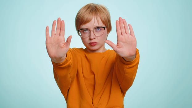 Young woman say No hold palm folded crossed hands in stop gesture, warning of finish, prohibited access, declining communication, body language, danger. Girl on blue background. People lifestyles