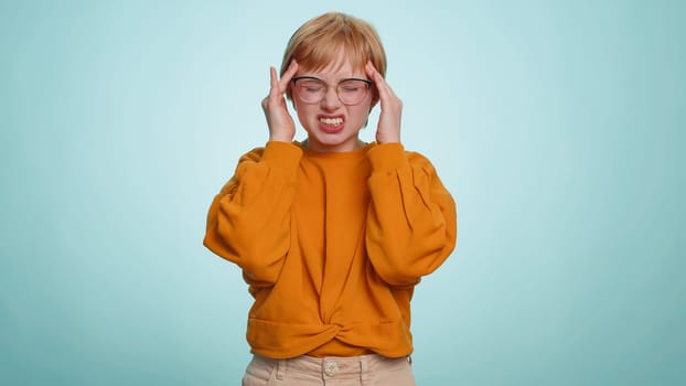 Pretty short haired woman in sweater rubbing temples to cure headache problem, suffering from tension, migaine, stress, grimacing in pain, high blood pressure isolated alone on blue wall background