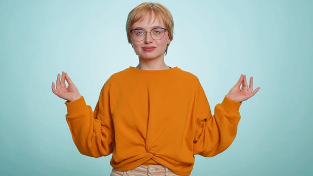 Keep calm down, relax, inner balance. Young woman in glasses breathes deeply with mudra gesture, eyes closed, meditating with concentrated thoughts, peaceful mind. Girl isolated on blue background