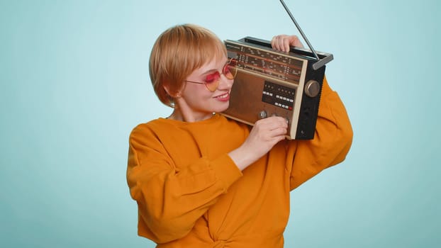 Woman in sunglasses using retro tape record player to listen music, disco dancing of favorite track, having fun, entertaining, fan of vintage technologies. Blonde girl isolated on blue background