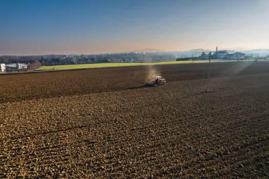 farmer driving a crawler tractor drags a cloud of dust behind, ploughing, power harrowing surface crust breaking to facilitate the birth and seeding of plants on dry soil
