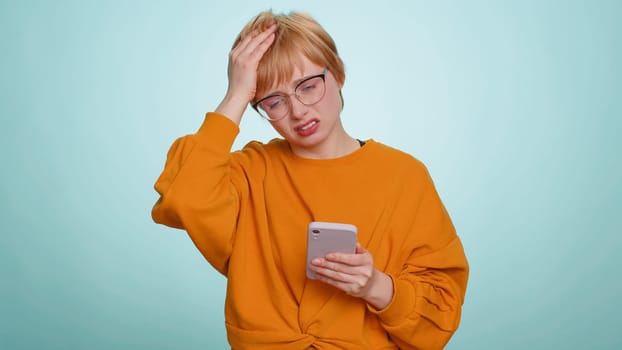 Woman use mobile phone smartphone typing browsing, loses becoming surprised sudden lottery results, bad fortune, loss, fail. Pretty blonde girl isolated alone on blue studio wall background, indoors