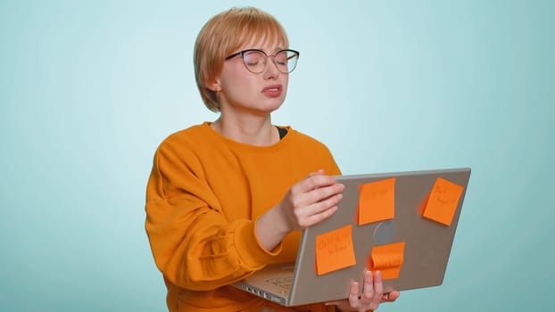 Exhausted freelancer woman in glasses with pasted sticker notes use laptop computer having concentration problem creative crisis. Nervous girl confused by big routine work loading on blue background