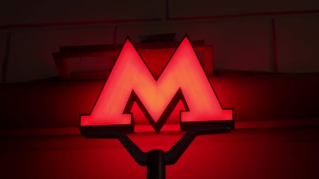 The metro symbol glows on the night street. A large red letter M indicating a subway close-up. 4k