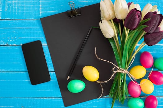 Easter eggs and tulips on blue wooden planks. Top view. Copy space