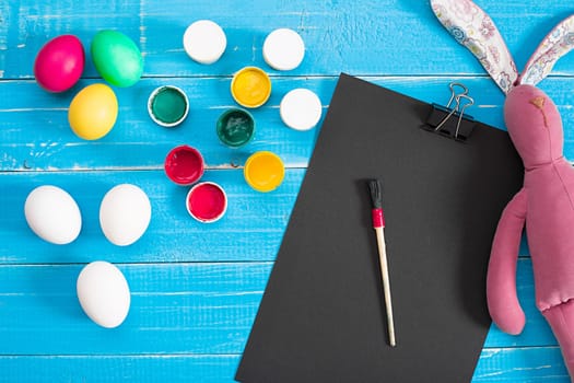 Colorful easter eggs, brush and paint on wooden board background with space. Top view