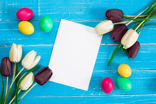Colorful easter eggs and tulips on blue rustic wooden background. Still life. Top view. Copy space