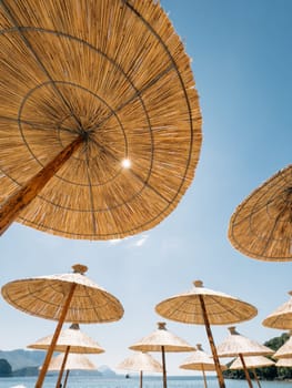 Straw sun umbrellas on the beach by the sea against the blue sky. High quality photo