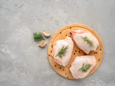 Top view with copy space. Raw chicken thighs on cutting board with ingredients for cooking at grey concrete kitchen table.