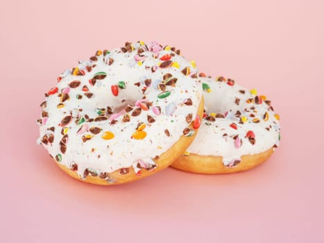 Unhealthy calorie food. Two circle donut with white icing and choclate rainbow sprinkles on a trendy pink background. Tasty doughnutdonut, vertical view. Sweet food leftlovers.