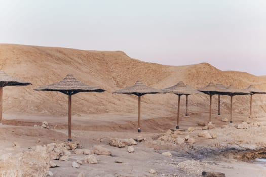 Sandy and rocky coast with palm beach umbrellas in paspel colors. Desolate resort beidge beach on the coast shore of Red Sea. Sharm el Sheikh, Sinai, Egypt, Asia. Travel in the time of coronavirus