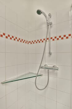 a shower with red and white tiles on the wall behind it, there is a glass shelf in the corner