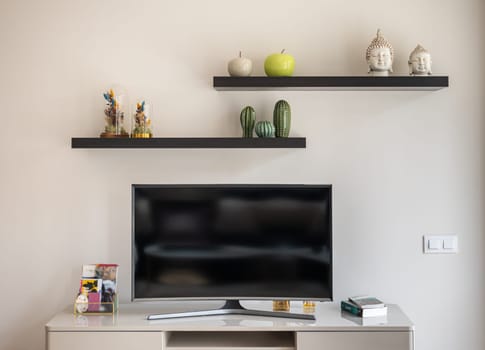 Close-up of a home theater tv on a white wall with shelves and stylish interior accessories. The concept of living room for a young family or hotel. Copyspace.