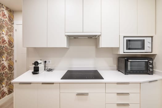 Frontal shot of a white kitchen unit with functional appliances and a convection hob. The concept of convenience and simplicity in interior design for young families.