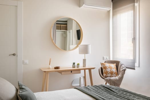 View from the bed is a cozy light-colored bedroom with wooden eco-furniture, console and mirror in a new apartment for a young family. The concept of a comfortable apartment.