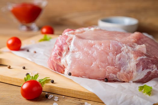 A piece of raw pork meat on a cutting board. Tomatoes, ketchup