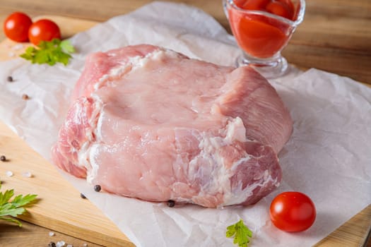 A piece of raw pork meat on a cutting board. Tomatoes, ketchup