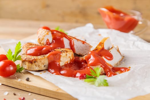 Slices of roast pork meat with tomato and ketchup on a wooden board