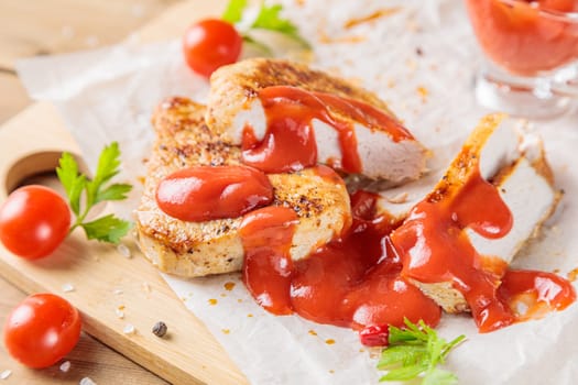 Slices of roast pork meat with tomato and ketchup on a wooden board. Top view