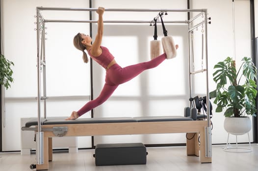 Beautiful asian woman in pink sportswear doing pilates on bed reformer