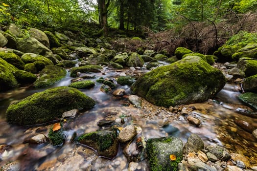 Beautiful small waterfall full of small and big rocks and stones with green trees around next to mountain trail in Giant mountains 