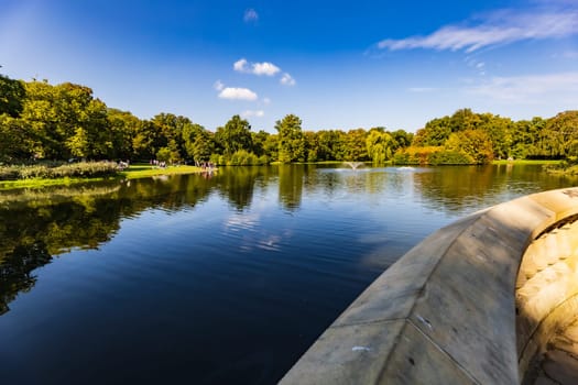 Beautiful sunny panorama of big lake with small fountains at center and green trees and bushes around in city South park 