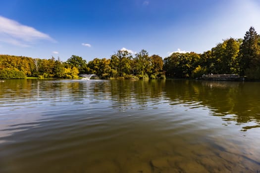 Beautiful sunny panorama of big lake with small fountains at center and green trees and bushes around in city South park 