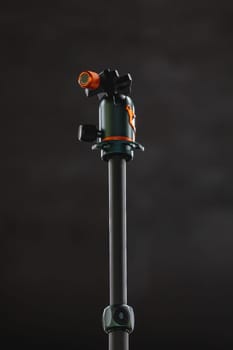 Gray central column of photo tripod with green and orange ballhead on top