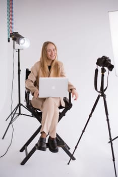 A business woman videographer producer assistant in a suit is working, typing on a laptop and sitting on a chair. Video Production studio, tripod camera