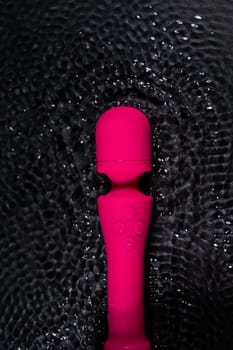 The pink dildo creates a vibration on the surface of the water. Sex toy on a black background