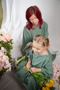 Amazing pretty mother and daughter having fun with flowers in 8 March or in Mother's day. Red haired mom and small little blonde girl having lovely free time on white background in studio