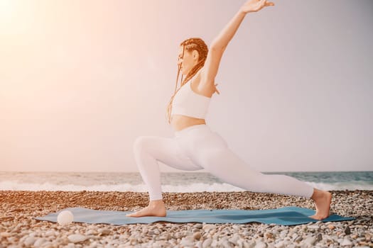 Woman yoga sea. Well looking middle aged woman with braids dreadlocks in white leggings and tops doing stretching pilates on yoga mat near sea. Female fitness yoga routine concept. Healthy lifestyle