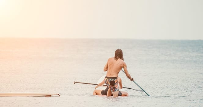 Sea woman and man on sup. Silhouette of happy young woman and man, surfing on SUP board, confident paddling through water surface. Idyllic sunset. Active lifestyle at sea or river