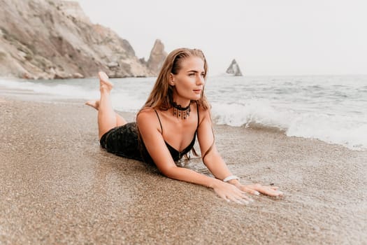 Woman travel sea. Young Happy woman in a long red dress posing on a beach near the sea on background of volcanic rocks, like in Iceland, sharing travel adventure journey