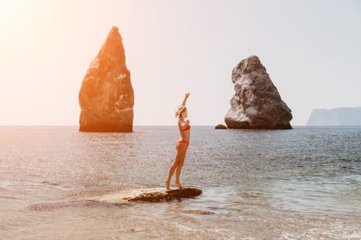 Woman travel sea. Young Happy woman in a long red dress posing on a beach near the sea on background of volcanic rocks, like in Iceland, sharing travel adventure journey