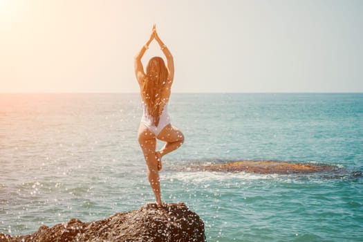 Woman sea yoga. Back view of free calm happy satisfied woman with long hair standing on top rock with yoga position against of sky by the sea. Healthy lifestyle outdoors in nature, fitness concept