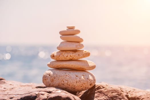 Pyramid stones on the seashore with warm sunset on the sea background. Happy holidays. Pebble beach, calm sea, travel destination. Concept of happy vacation on the sea, meditation, spa, calmness.