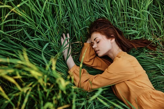 a close horizontal photo of a pleasant woman in a long orange dress resting lying in the tall grass with her eyes closed in sunny weather at sunset with her arms outstretched. Street photography,. High quality photo
