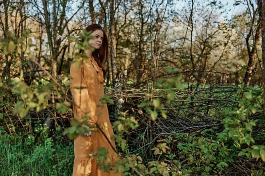 a beautiful, slender woman with long hair walks in the shade near the trees, dressed in a long orange dress, enjoying the weather and the weekend. The theme of privacy with nature, horizontal photography on the street. High quality photo