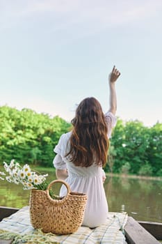 a woman sits on a blanket near the lake with her hands raised above her head and looks at the view. High quality photo