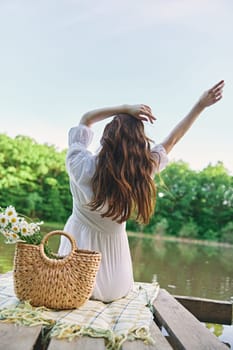 a woman sits on a blanket near the lake with her hands raised above her head and looks at the view. High quality photo